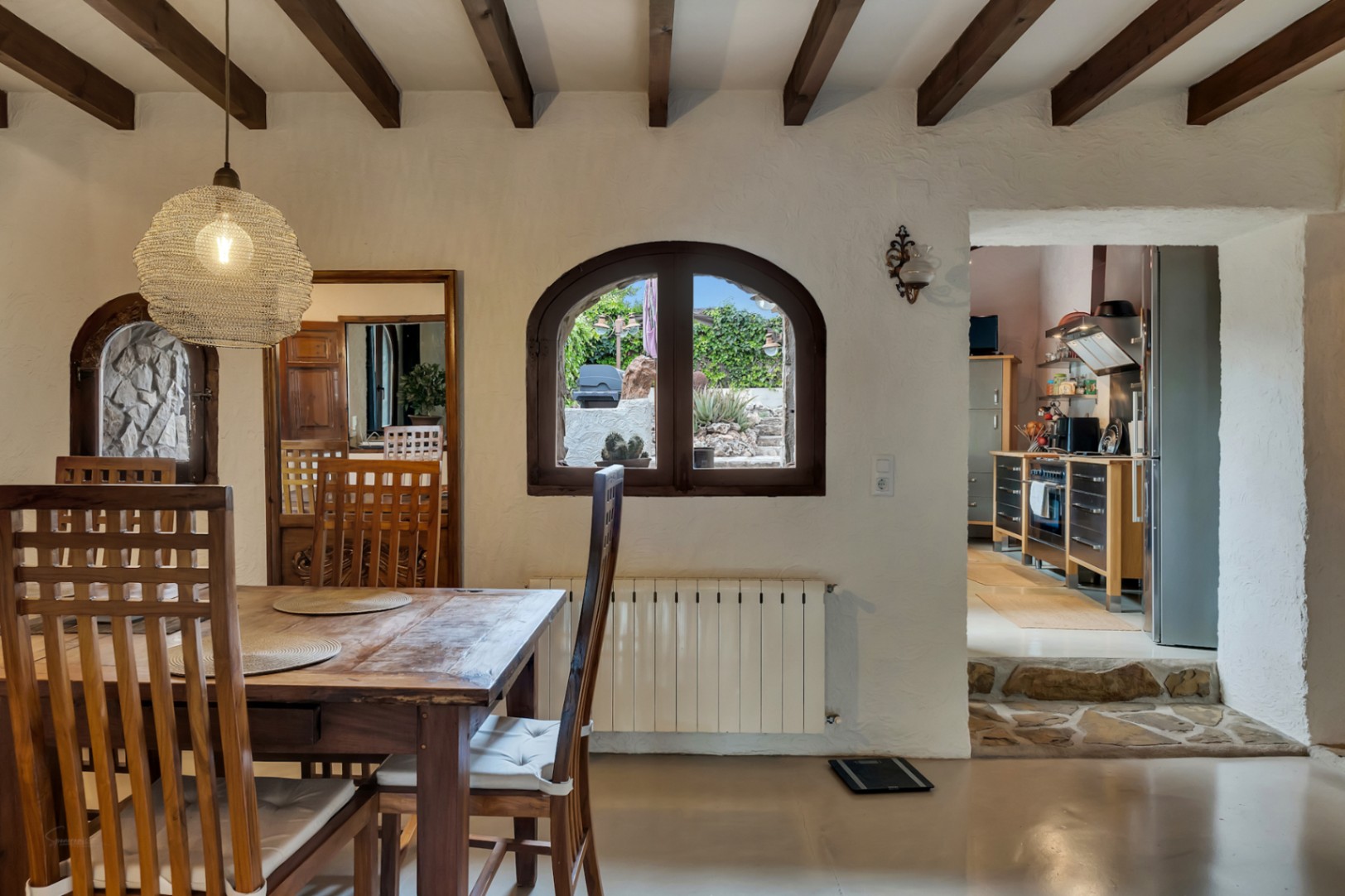 Comedor rústico con vigas de madera vista, mesa de madera maciza y acceso a la cocina mediante escalones de piedra natural.