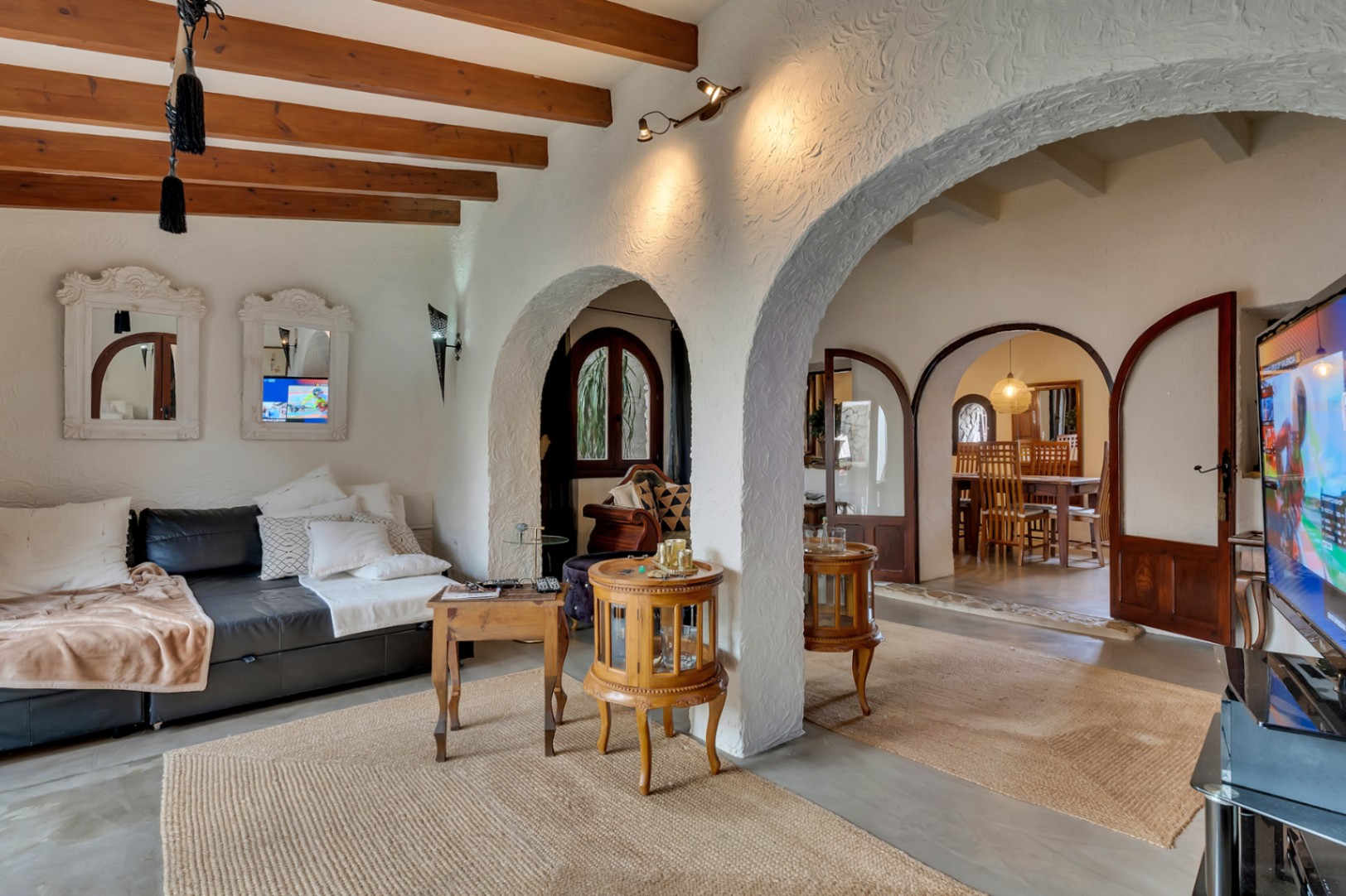 Salón con vigas de madera vista, arcos mediterráneos de pared texturizada y suelos con alfombras de yute que conectan visualmente con el comedor.
