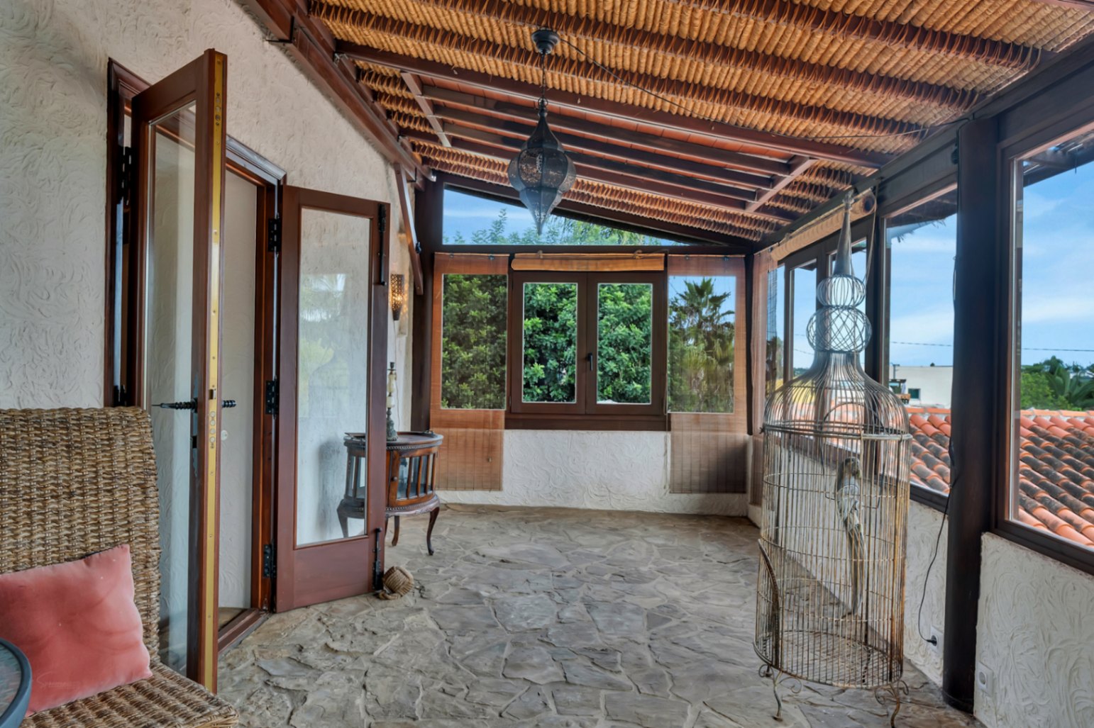 Terraza acristalada con suelo de piedra natural, techo de vigas de madera con cañizo y una lámpara de estilo marroquí con vistas a los tejados tradicionales.