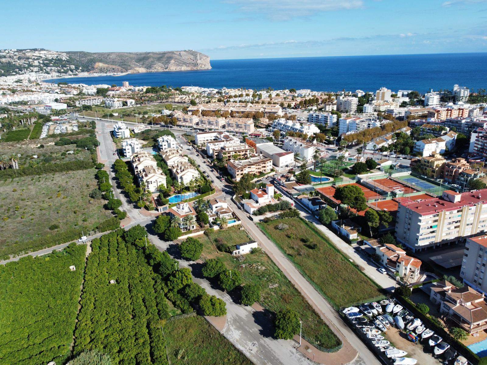 Vista aérea del solar rectangular junto a zonas agrícolas, destacando su proximidad al Club de Tenis y vistas panorámicas hacia la bahía de Jávea.