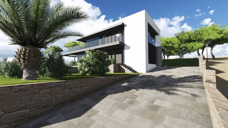 Vista exterior de la villa moderna con rampa de acceso empedrada, muros de piedra natural, fachada blanca con barandillas de cristal y vegetación mediterránea.