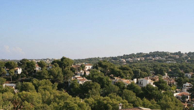 Vistas panorámicas desde la parcela hacia un valle residencial con villas blancas tradicionales y densos bosques de pinos mediterráneos.