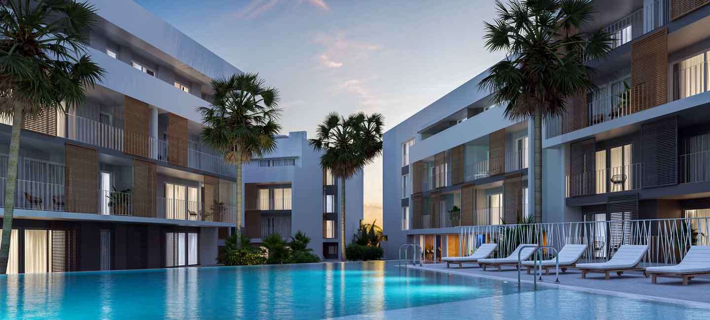 Zona de piscina comunitaria al atardecer, con tumbonas, palmeras y bloques de apartamentos modernos con persianas de madera y balcones de cristal.