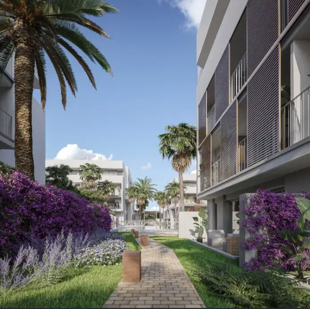 Un sendero de piedra recorre los jardines comunitarios con buganvillas púrpuras, palmeras y edificios modernos equipados con persianas de lamas verticales.