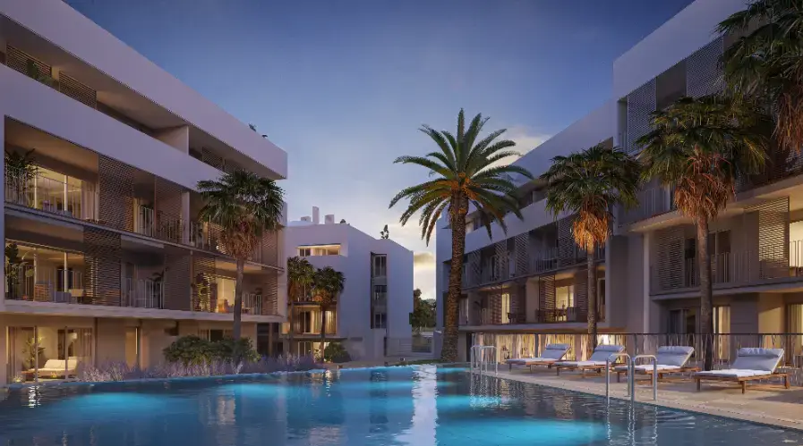 Vista exterior de la piscina comunitaria al atardecer, con iluminación subacuática, tumbonas y fachadas blancas modernas con celosías de privacidad.