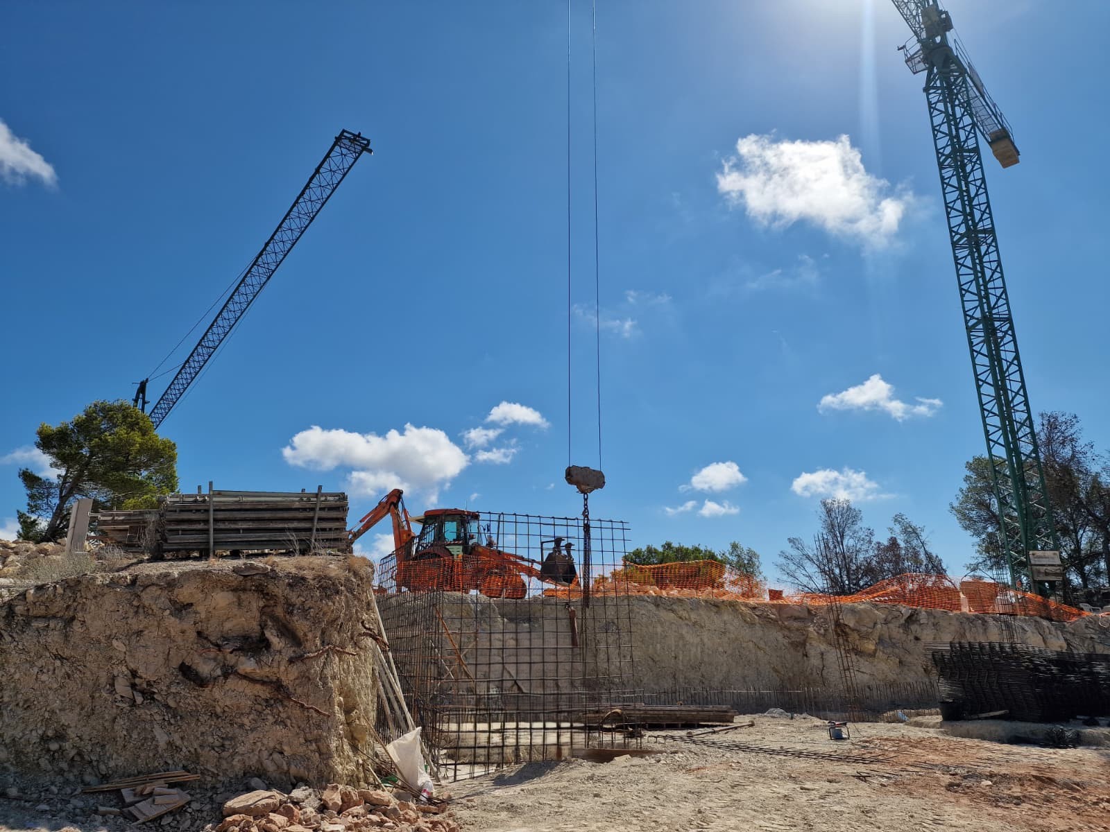 Avance de obra en Moraira que muestra la excavación del terreno, el armado de cimentación con acero y el despliegue de grúas y maquinaria pesada.
