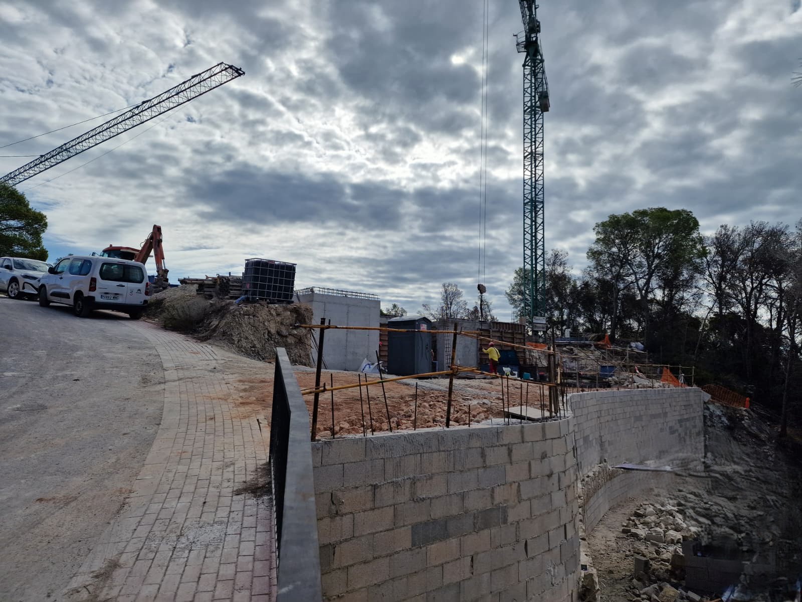 Estado de las obras en Moraira, destacando los muros de contención curvos, el acceso pavimentado y la maquinaria pesada durante la fase inicial de estructura.