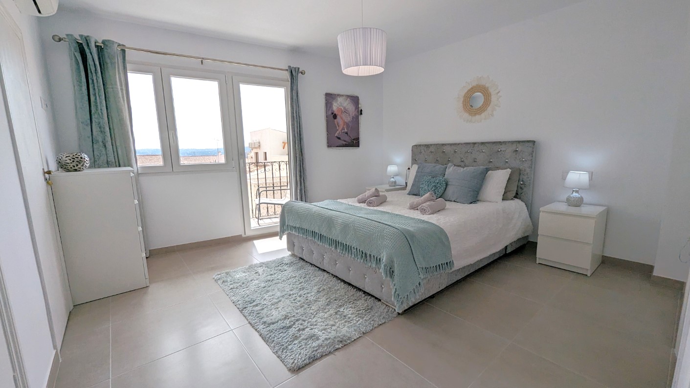 Dormitorio principal con cabecero tapizado, acceso directo a terraza privada mediante puertas acristaladas y suelos de gres en tonos neutros.