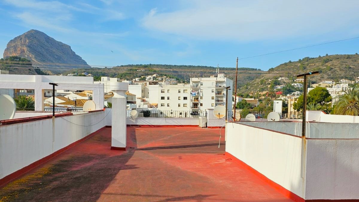 Terraza comunitaria en la azotea con suelo rojo y vistas despejadas al macizo del Montgó y al entorno urbano de Jávea bajo un cielo despejado.