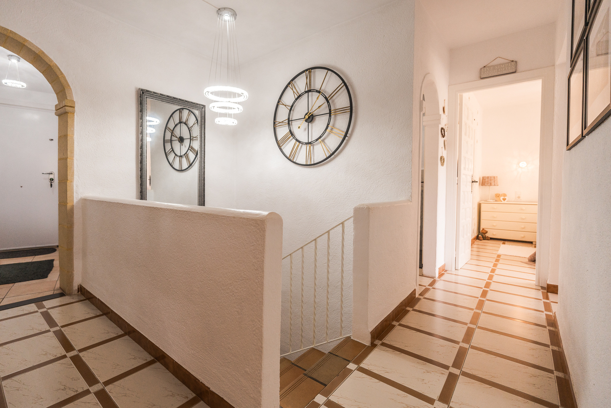 Distribuidor con arco de piedra tosca, suelos cerámicos decorados y una moderna lámpara LED de anillos sobre la escalera que comunica ambas plantas.