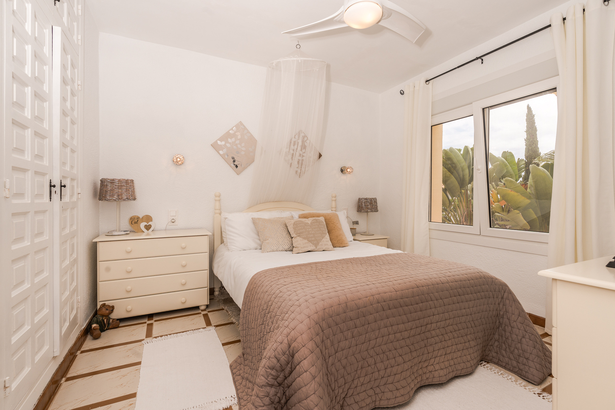 Dormitorio luminoso con armarios empotrados de cuarterones, ventilador de techo y ventanas de doble acristalamiento con vistas al jardín y suelo cerámico tradicional.