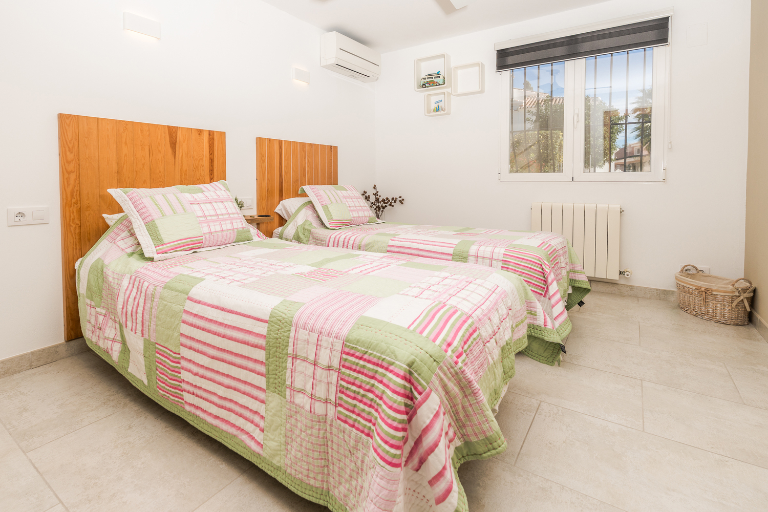 Dormitorio doble con cabeceros de madera natural, suelos cerámicos y aire acondicionado. Dispone de ventana con rejas de seguridad y calefacción por radiador.