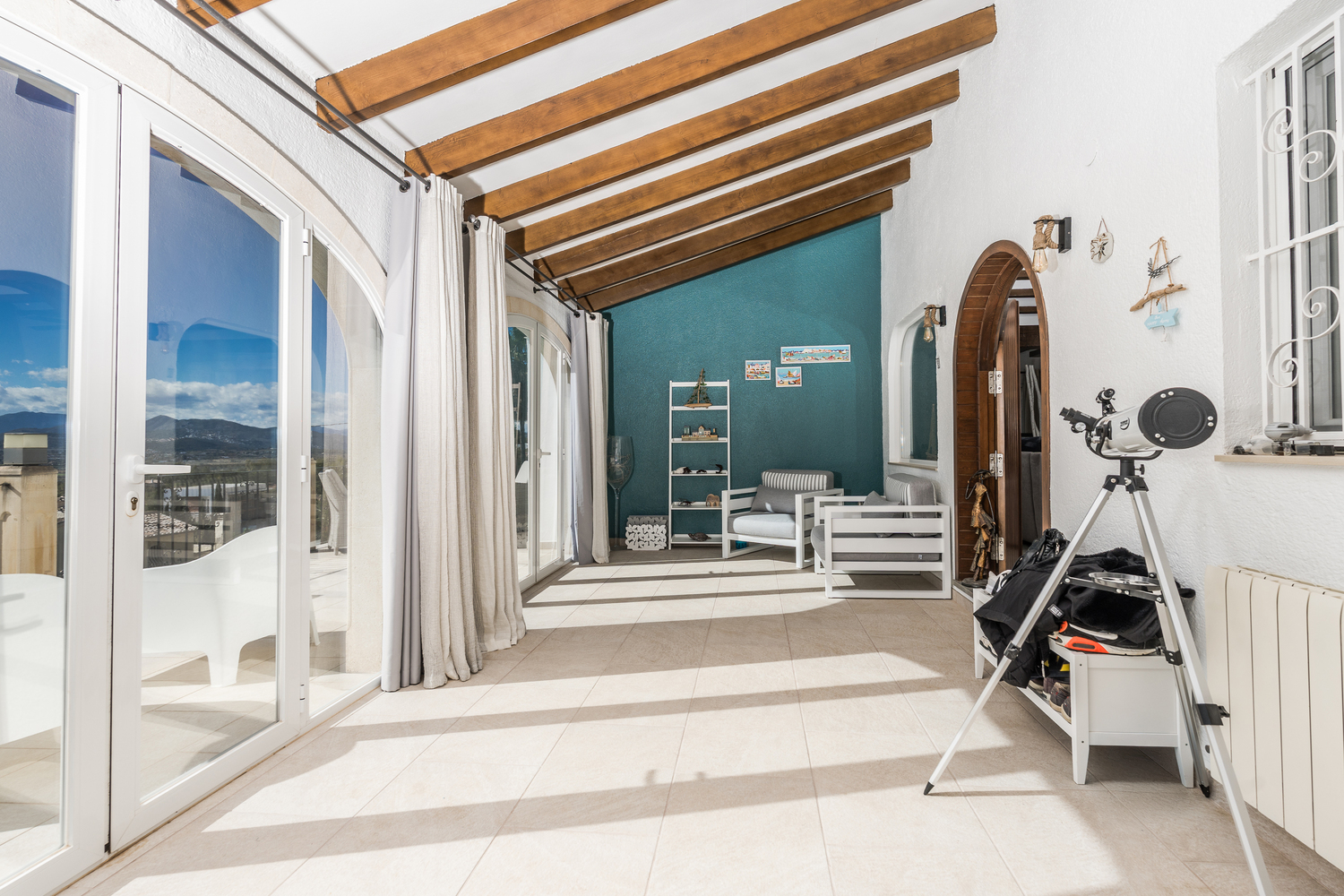 Naya acristalada con vigas de madera a la vista, suelo de baldosas y amplios ventanales que ofrecen vistas panorámicas a las montañas y acceso exterior.