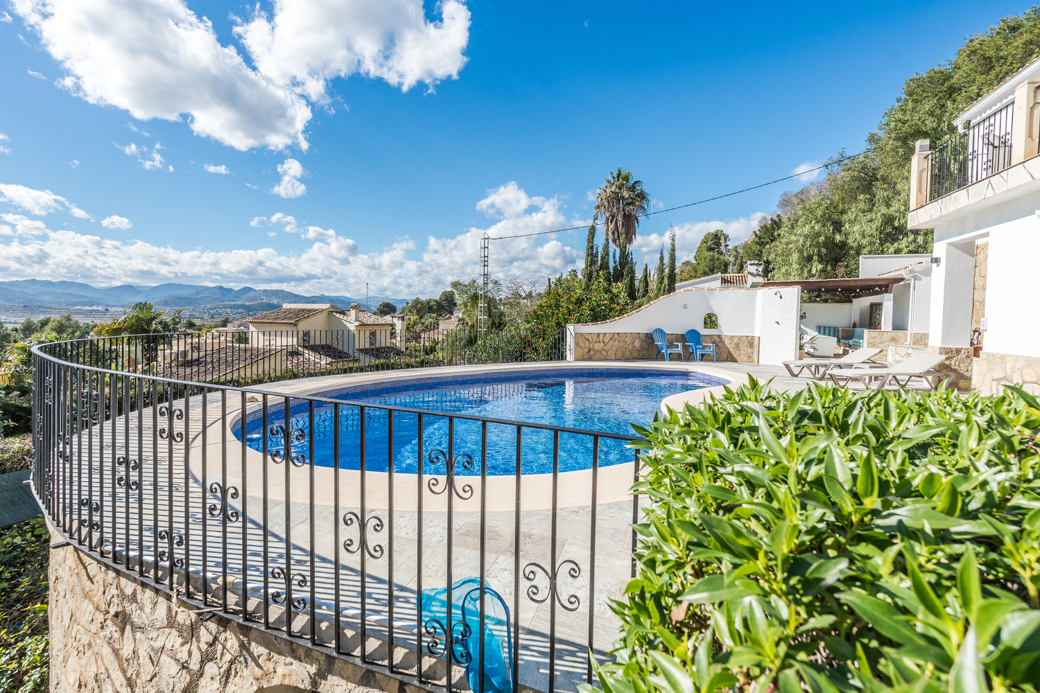 Terraza elevada con piscina en forma de riñón, barandilla de hierro forjado y vistas panorámicas al valle y las montañas circundantes.