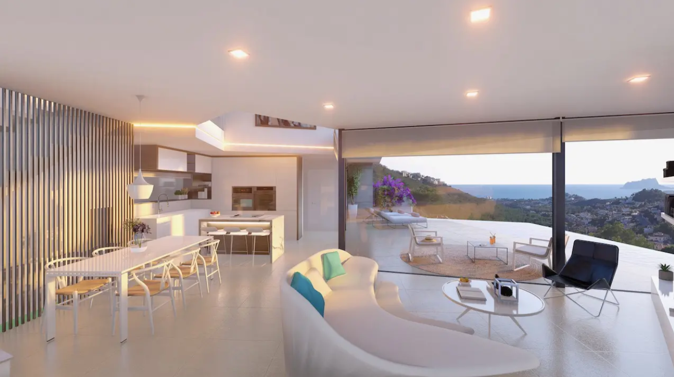 Zona de estar de concepto abierto con sofá curvo, comedor y cocina integrada. Amplios ventanales conectan el interior con una terraza con vistas despejadas al litoral mediterráneo.