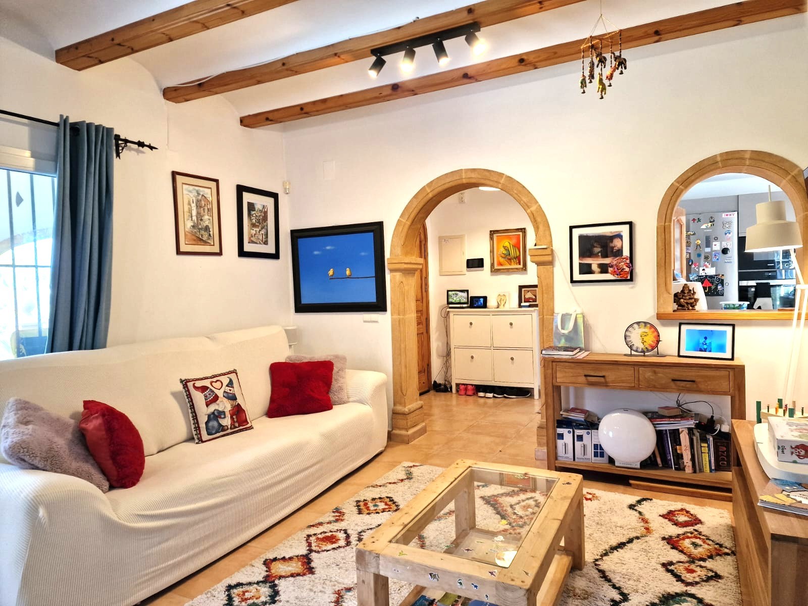 Salón con vigas de madera a la vista, arcos de piedra Tosca tradicional y una distribución luminosa que conecta con la cocina mediante una apertura arqueada.