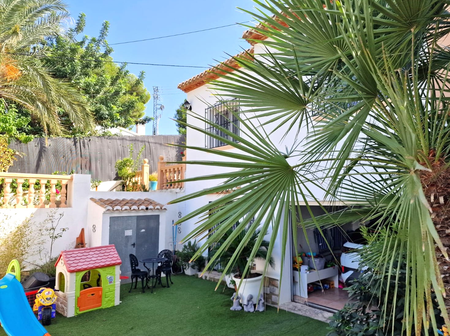 Vista exterior del nivel inferior que muestra una zona de juegos infantil sobre césped artificial, un cobertizo de almacenamiento y el acceso al garaje.