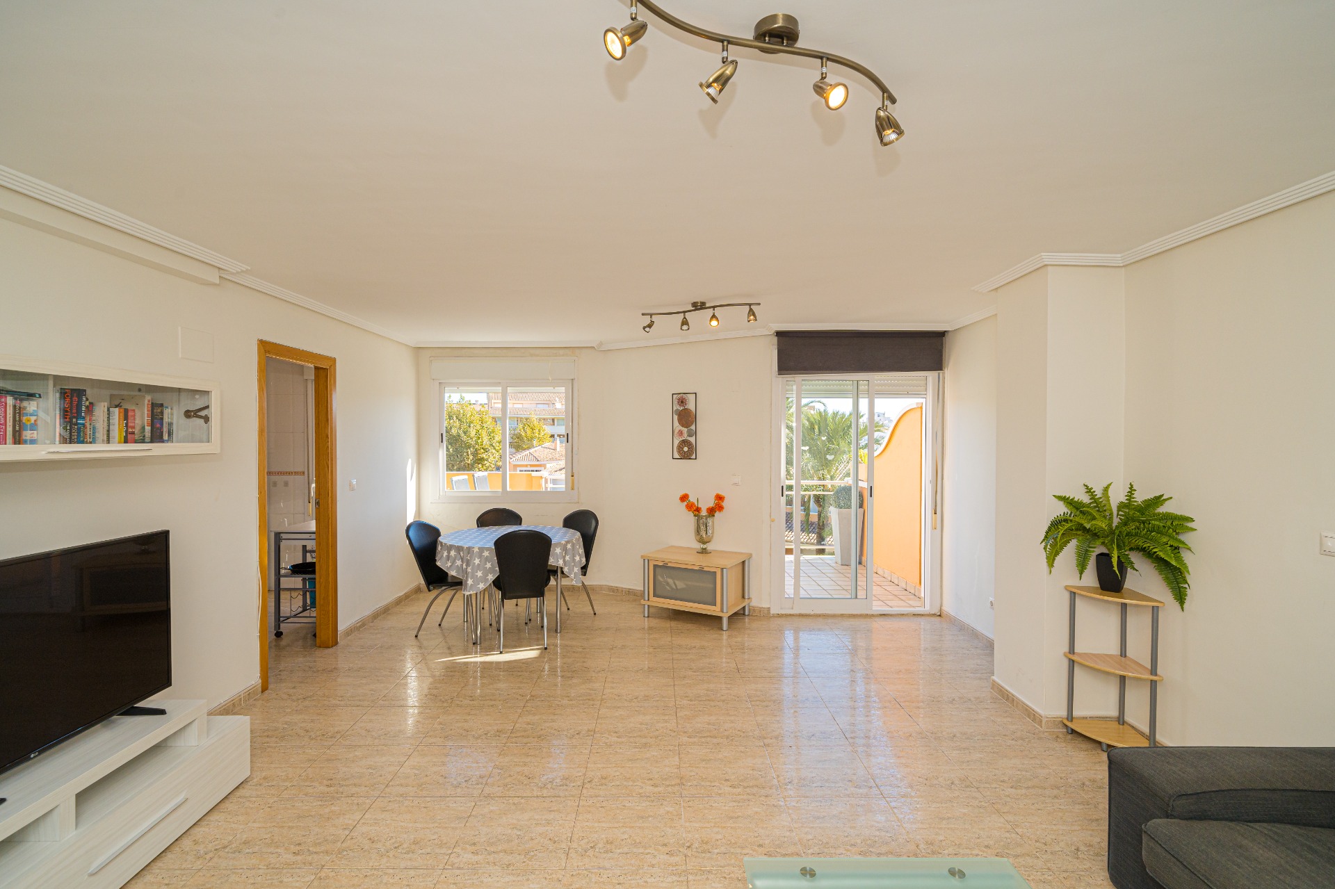 Amplio salón-comedor con suelos de gres, iluminación mediante focos y acceso directo a una terraza privada a través de puertas correderas de cristal.