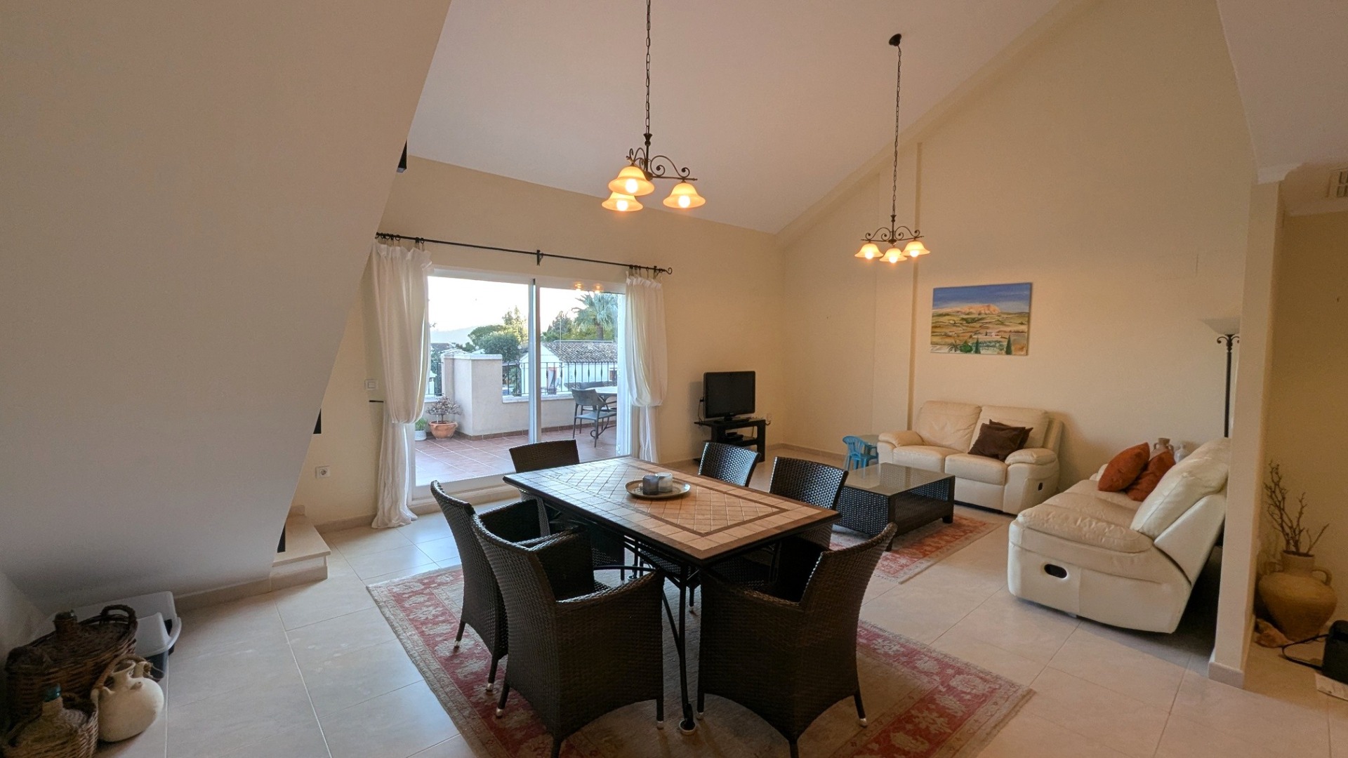 Amplio salón-comedor con techos altos abuhardillados, suelos de gres y acceso directo a una terraza privada mediante grandes ventanales correderos.