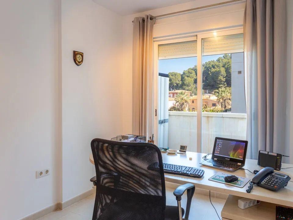 Despacho luminoso con escritorio y silla ergonómica, equipado con ventanales correderos que ofrecen vistas despejadas a las colinas de pinos circundantes.
