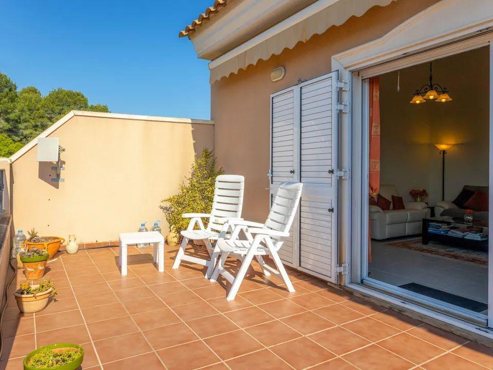 Terraza exterior con suelo de baldosas cerámicas, mobiliario de exterior y acceso directo al salón mediante puertas correderas con persianas mallorquinas blancas.