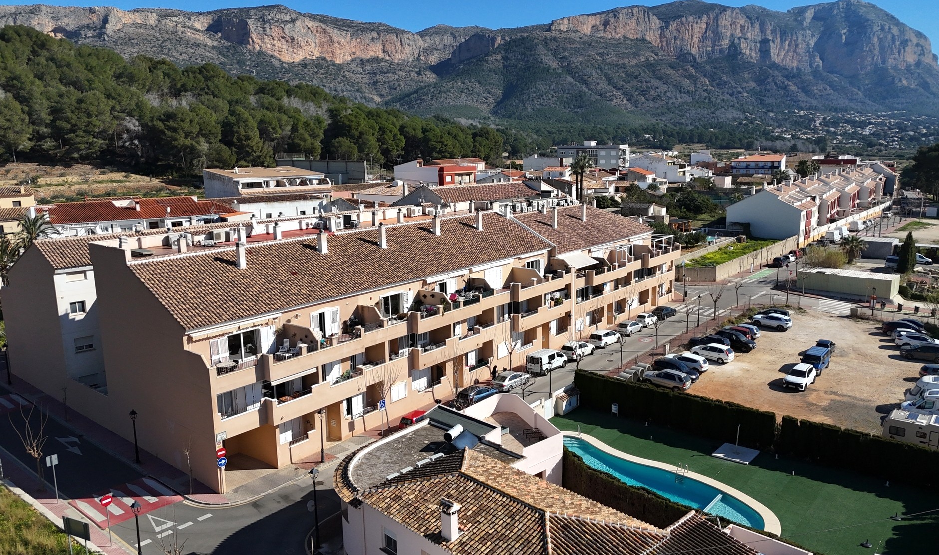 Vista elevada del complejo en Jesús Pobre, destacando la piscina comunitaria, los tejados de teja cerámica y las vistas al macizo del Montgó.