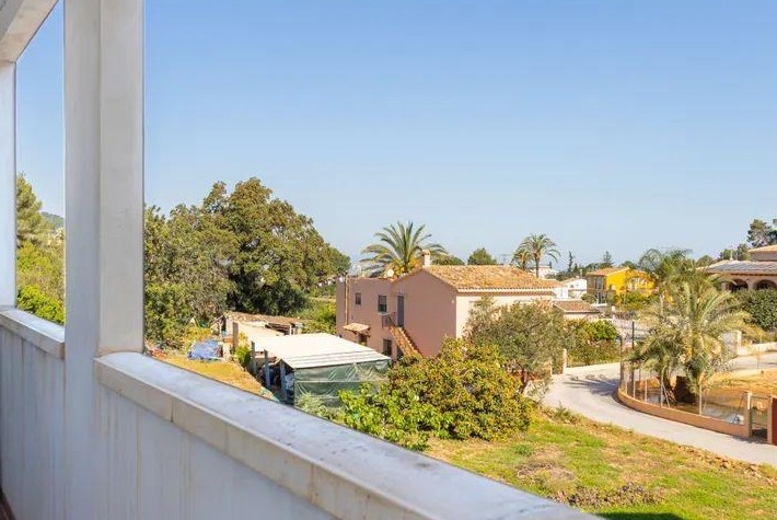 Vistas desde el balcón hacia el pueblo de Jesús Pobre, con arquitectura mediterránea, palmeras y cielos despejados sobre el paisaje rural circundante.