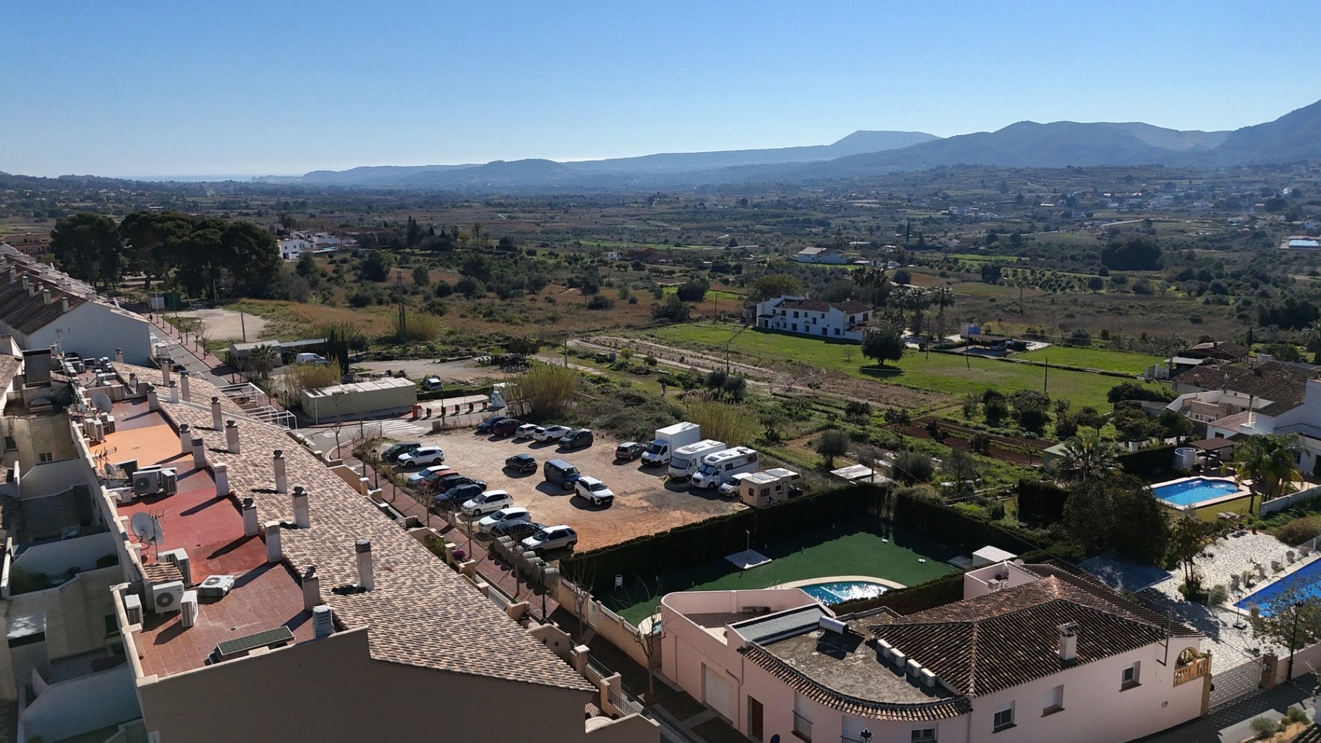 Vistas despejadas desde el ático hacia el campo, la zona de aparcamiento y las montañas circundantes bajo un cielo despejado.
