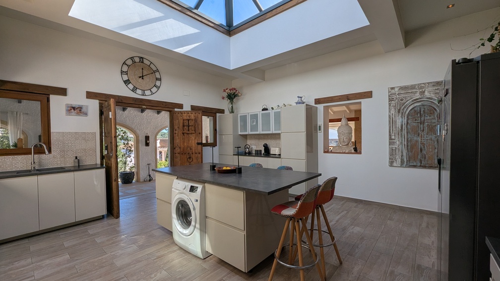 Cocina moderna con isla central y una gran claraboya que inunda el espacio de luz natural. Incluye carpintería de madera tradicional y acceso directo a la naya.