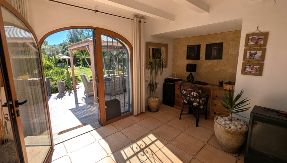Despacho luminoso con suelos de terracota, pared de piedra tosca y puertas de madera en arco que conectan directamente con la terraza y el jardín.