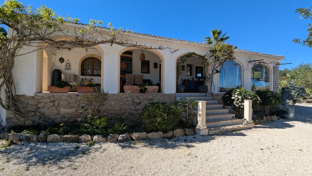 Fachada de estilo finca con naya de arcos tradicionales, base de piedra natural y escalinata de acceso integrada en un entorno mediterráneo.