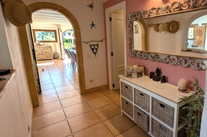 Pasillo de entrada con un arco de piedra Tosca tradicional, suelos de terracota y un espejo ornamentado sobre un mueble con cestas de mimbre.
