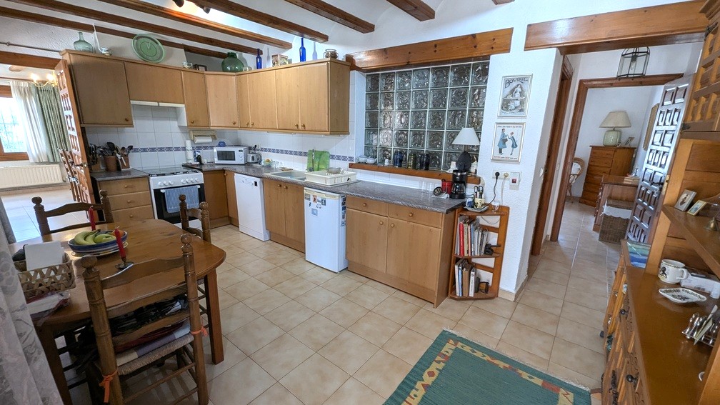Cocina de estilo tradicional con vigas de madera vistas, mobiliario de madera clara y una pared de bloques de vidrio que aporta luz natural al espacio.