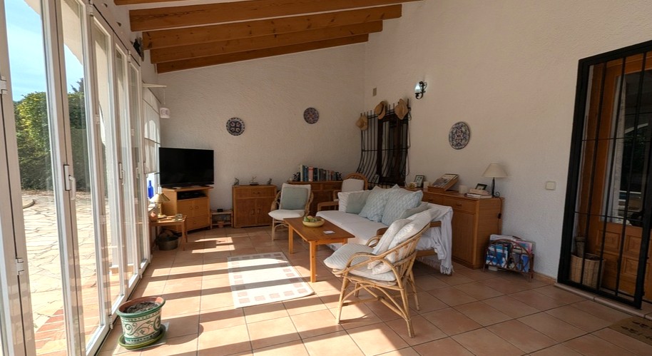 Naya acristalada con vigas de madera vista, suelos de terracota y amplios ventanales correderos que conectan con la terraza exterior.
