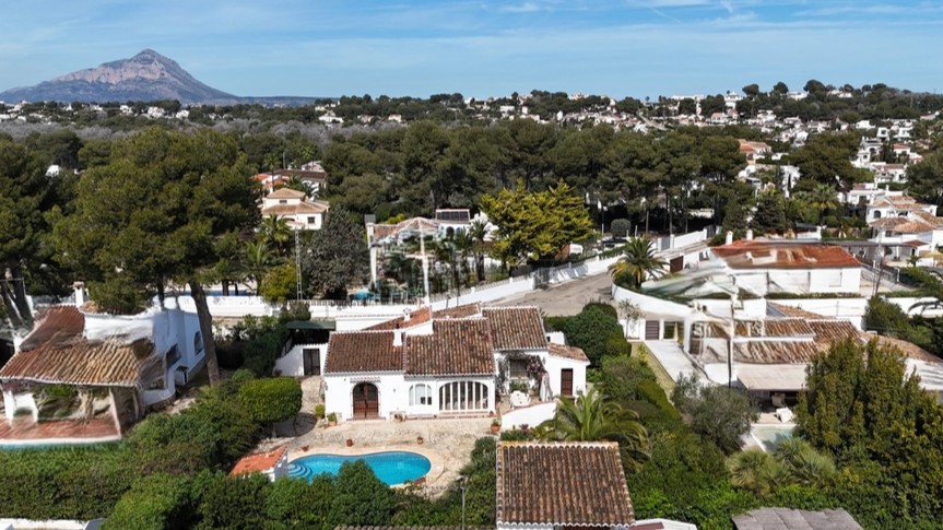 Vista aérea de la villa tradicional con piscina privada, tejados de teja cerámica y jardín maduro, destacando el monte Montgó al fondo.