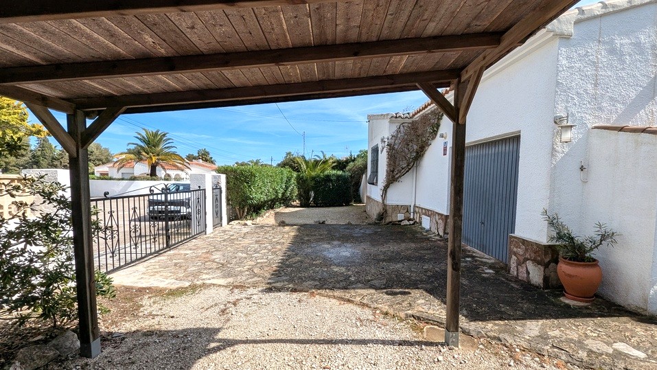 Vista desde el porche de madera que muestra la entrada empedrada, el garaje y la puerta de hierro forjado que da acceso a la propiedad.