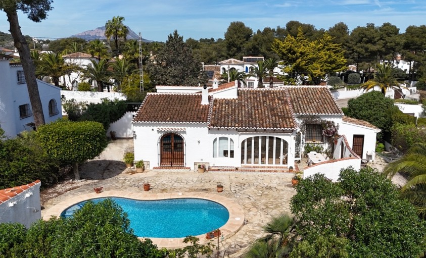 Vista elevada de la villa con piscina en forma de riñón, terraza de piedra y tejado tradicional, destacando el monte Montgó en el horizonte.
