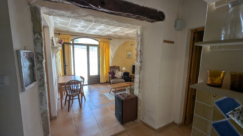 Arco tradicional de piedra Tosca con viga de madera que da paso a una estancia con suelos cerámicos y ventanales en arco hacia el exterior.