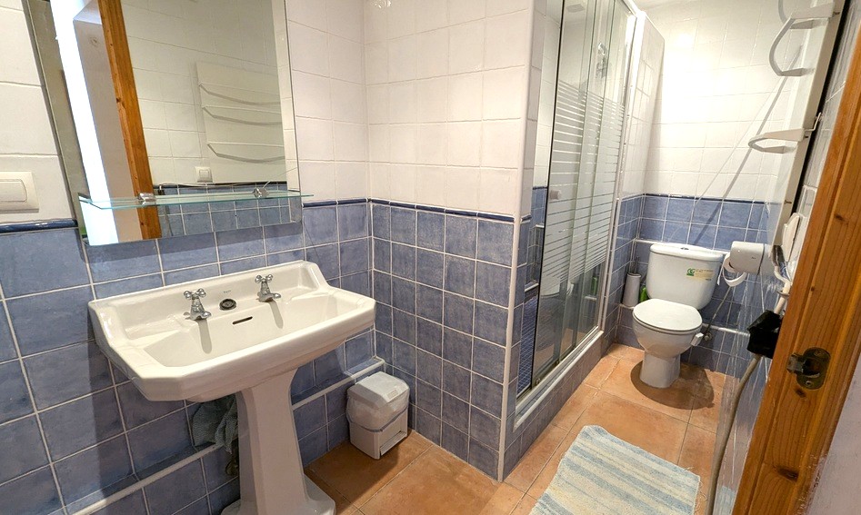 Baño de estilo tradicional con azulejos en azul y blanco, lavabo de pedestal clásico, suelo de terracota y ducha con mampara de cristal.