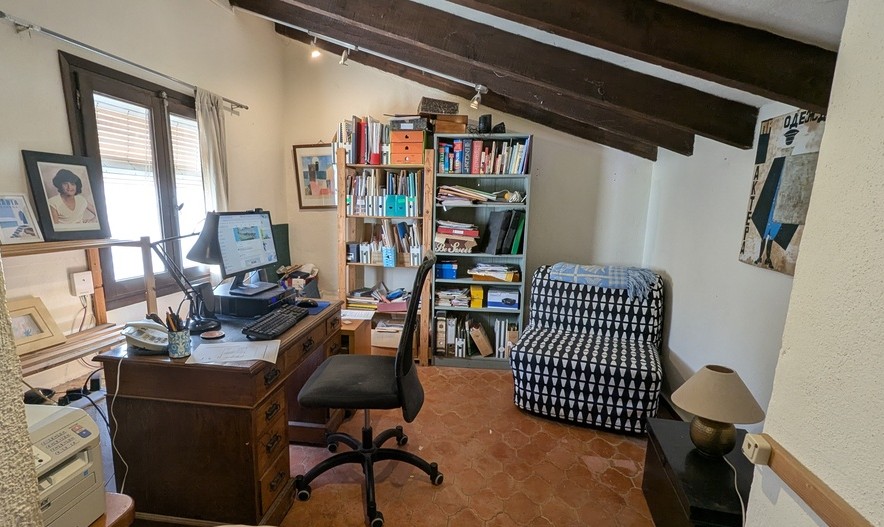 Despacho con suelos de terracota tradicionales, vigas de madera oscura a la vista en el techo inclinado y un escritorio de madera clásica junto a la ventana.
