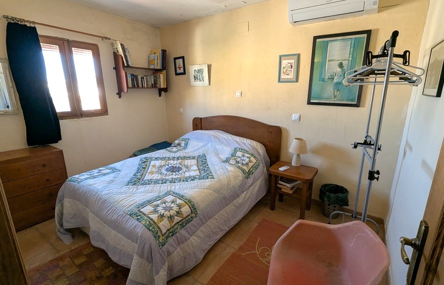 Dormitorio con mobiliario de madera, suelos de gres y aire acondicionado split. Incluye estantería de pared, cómoda clásica y luz natural desde una ventana de madera.