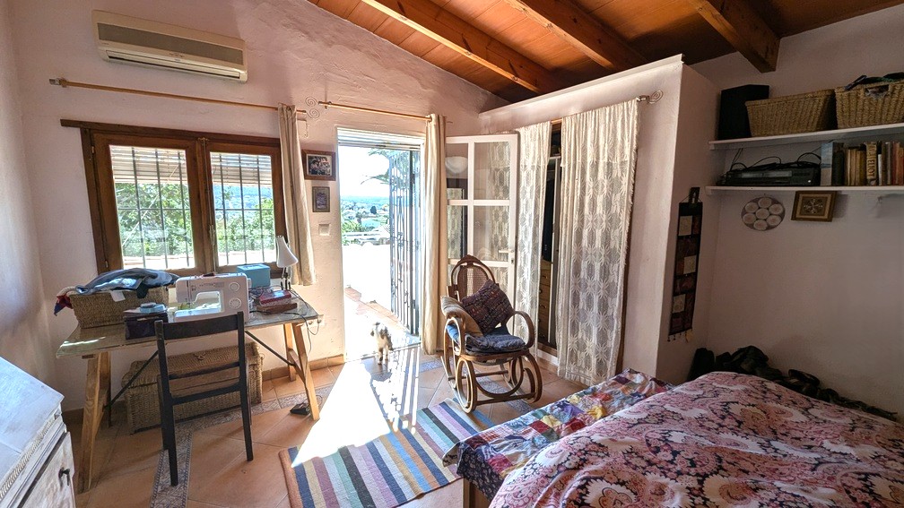 Dormitorio con vigas de madera a la vista, suelos de terracota y acceso directo a una terraza con vistas al campo. Dispone de aire acondicionado y zona de trabajo.