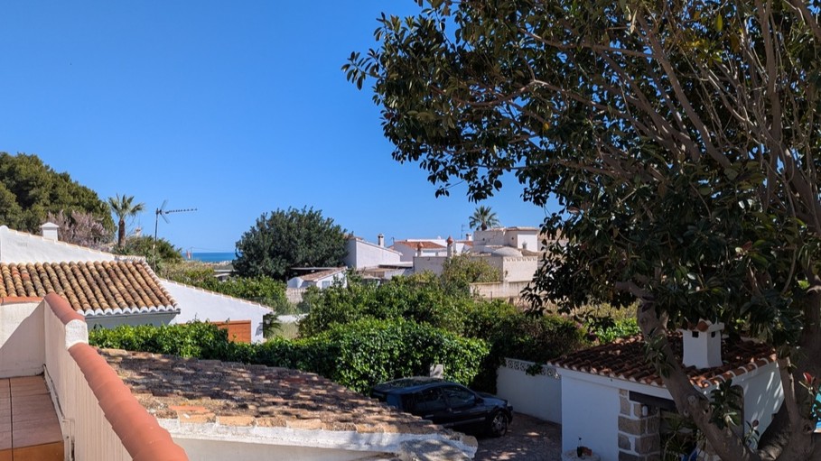 Vista desde la terraza superior que muestra los tejados tradicionales, el jardín arbolado y una perspectiva del mar Mediterráneo en el horizonte.