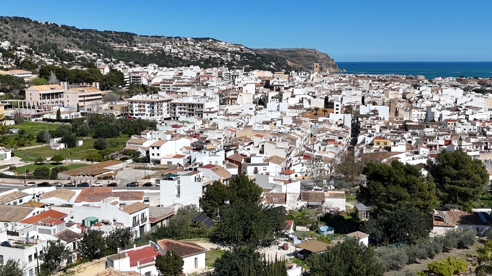 Vista panorámica elevada del casco antiguo de Jávea, que muestra las casas blancas tradicionales, el campanario de San Bartolomé y el mar Mediterráneo al fondo.