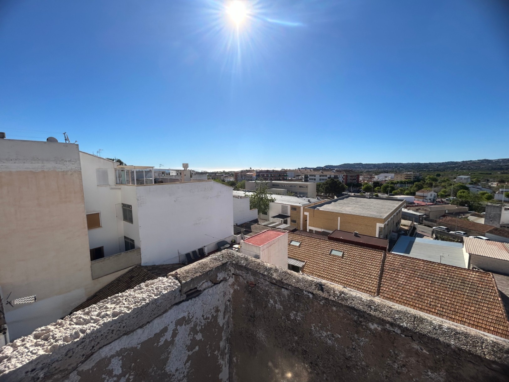 Vistas panorámicas desde la azotea hacia el casco urbano de Jávea y el mar Mediterráneo, destacando los tejados tradicionales y el entorno montañoso bajo un cielo despejado.