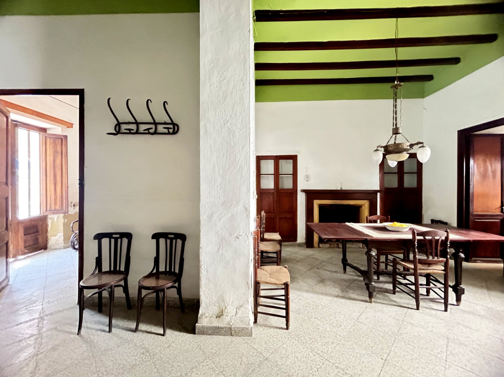 Salón-comedor tradicional con vigas de madera originales, techos altos en verde y chimenea clásica. Destacan el mobiliario de época y el acceso a estancias luminosas.