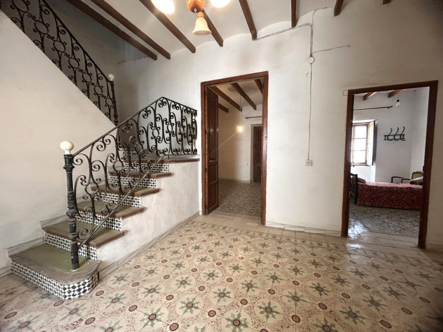 Vestíbulo principal con suelos hidráulicos originales, vigas de madera vista y una escalera señorial con barandilla de hierro forjado y azulejos decorativos.