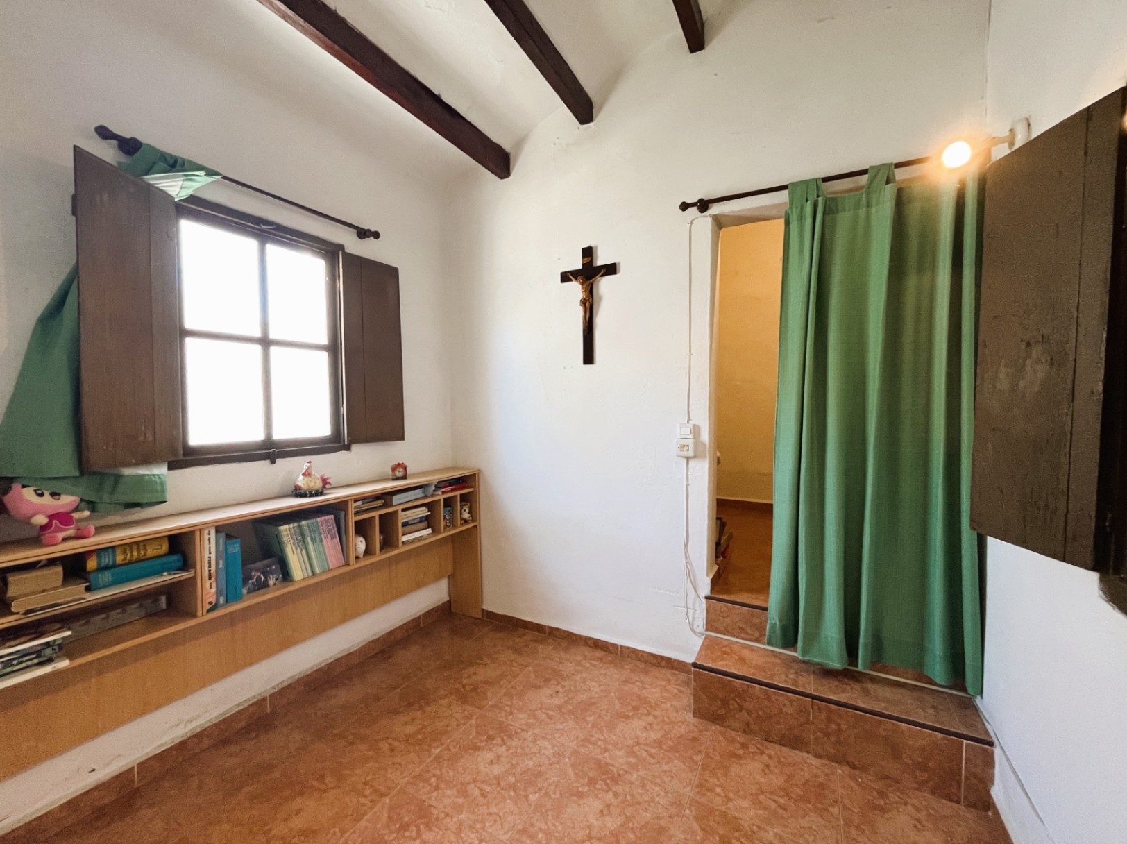 Estancia con vigas de madera oscura, suelos de gres y estantería bajo ventana de madera. Incluye un acceso elevado con peldaños cerámicos y cortina divisoria.