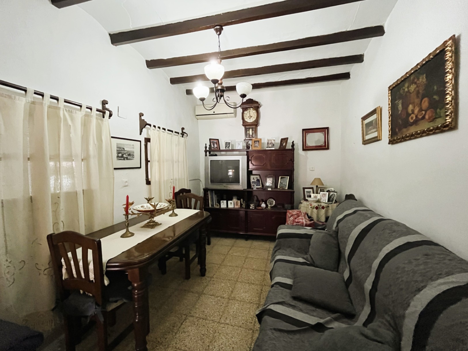 Salón-comedor tradicional con vigas de madera a la vista, suelos de terrazo y mobiliario clásico de madera oscura en el casco antiguo de Jávea.