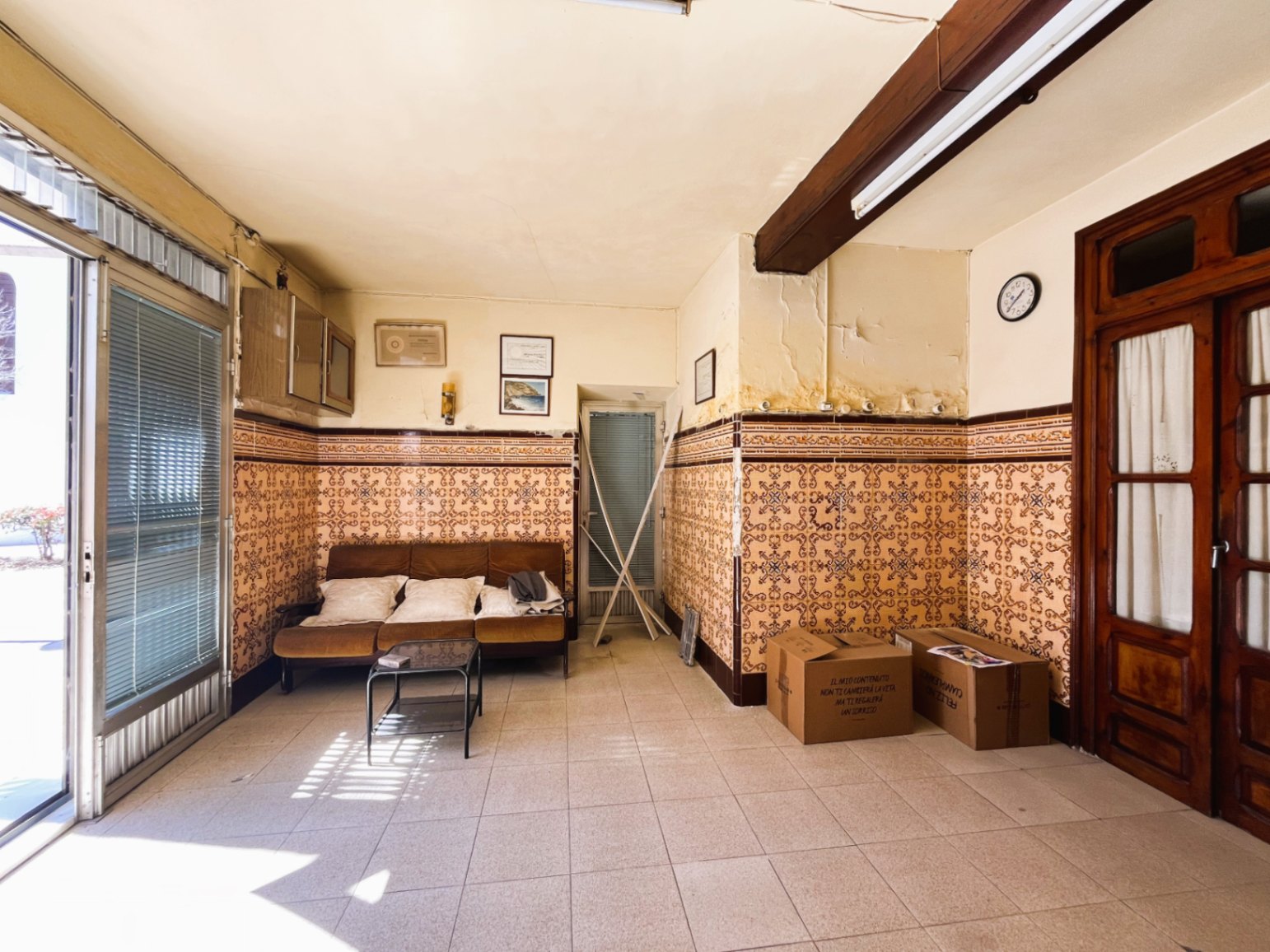 Salón de entrada con azulejos tradicionales, vigas de madera vista y una gran puerta acristalada que permite la entrada de abundante luz natural.